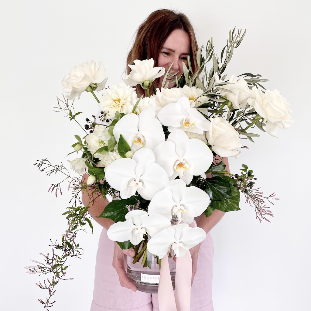 Bundall-florist-LULLY-&-ROSE-owner-with-vase-arrangement-of-white-phalaenopsis-orchids-roses-dahlias-jasmine-vine-and-olive-Gold-Coast